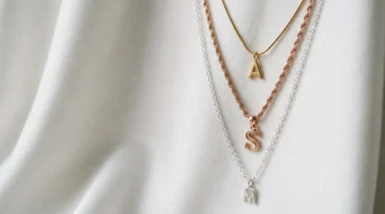 Composizione elegante di collane con iniziali sovrapposte in modo armonioso su fondo minimalista