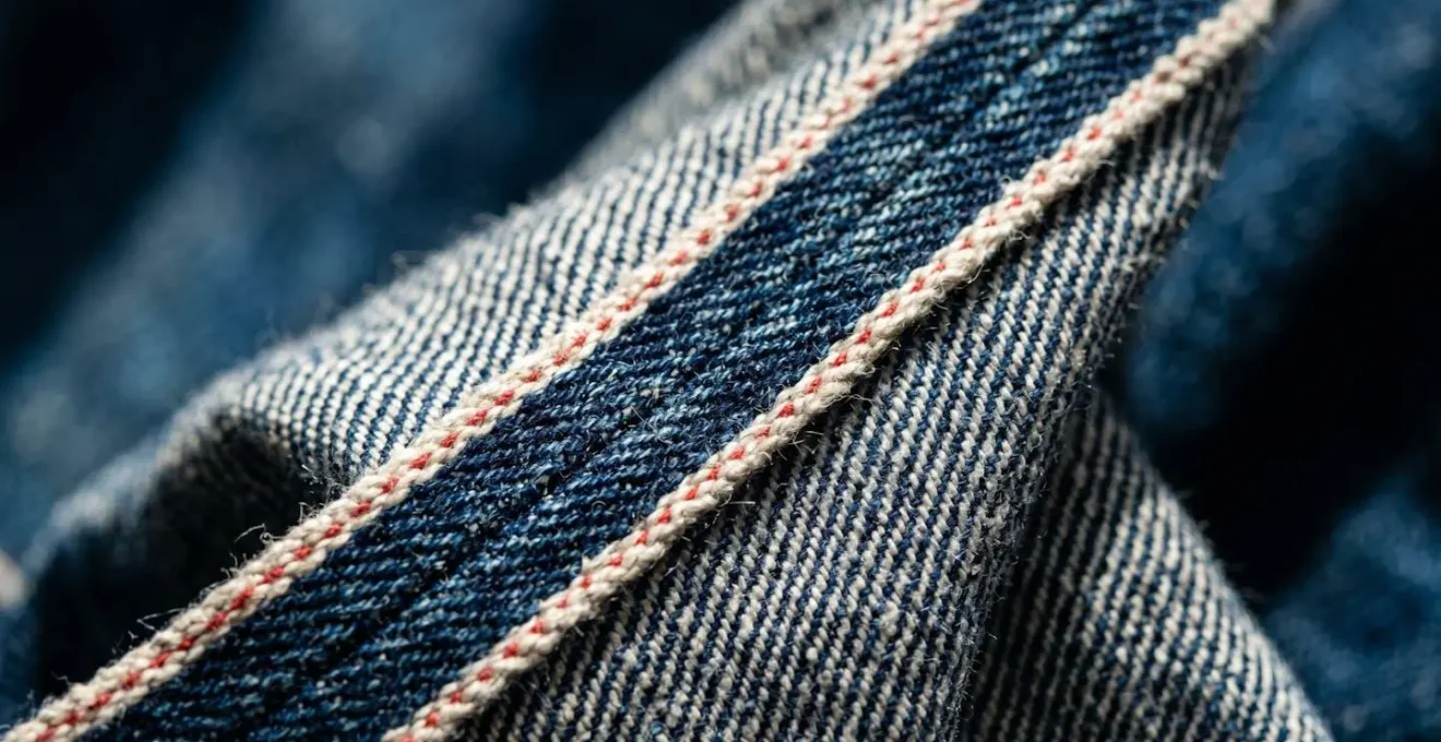 Dettaglio macro della tessitura densa del denim cimosato selvedge, con bordo caratteristico
