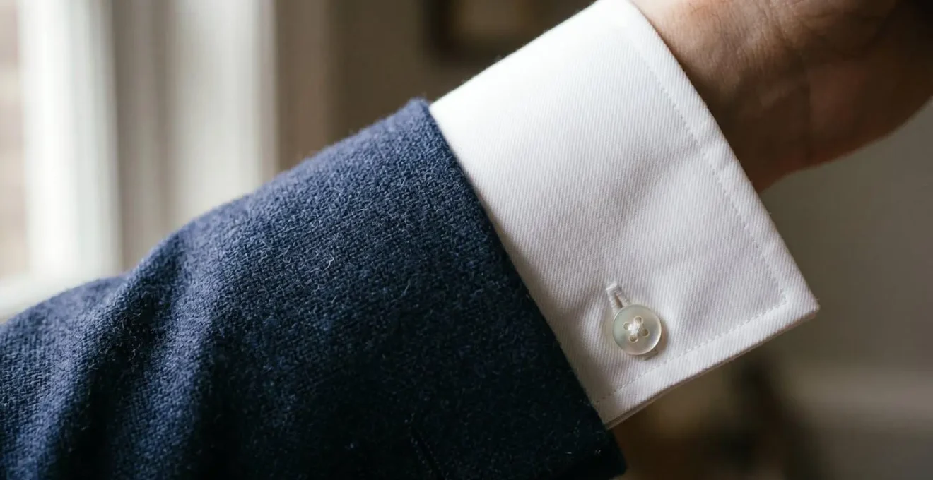 Dettaglio ravvicinato del polsino di una camicia bianca che spunta dalla manica di una giacca sartoriale blu navy
