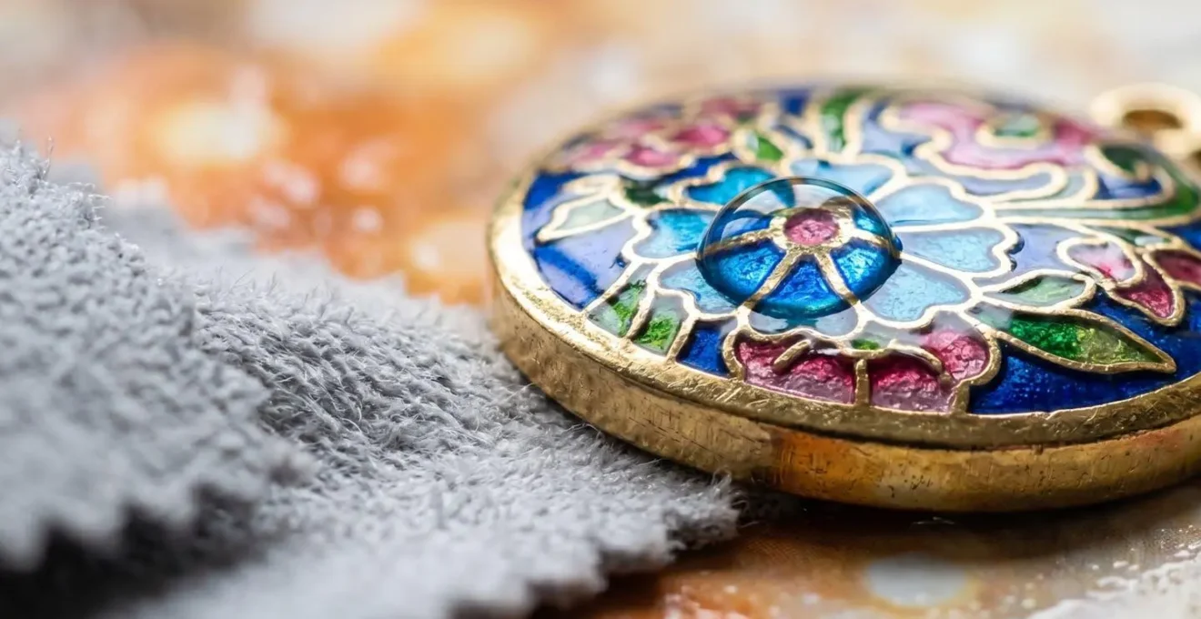 Dettaglio macro di un ciondolo smaltato colorato durante una pulizia delicata con panno morbido